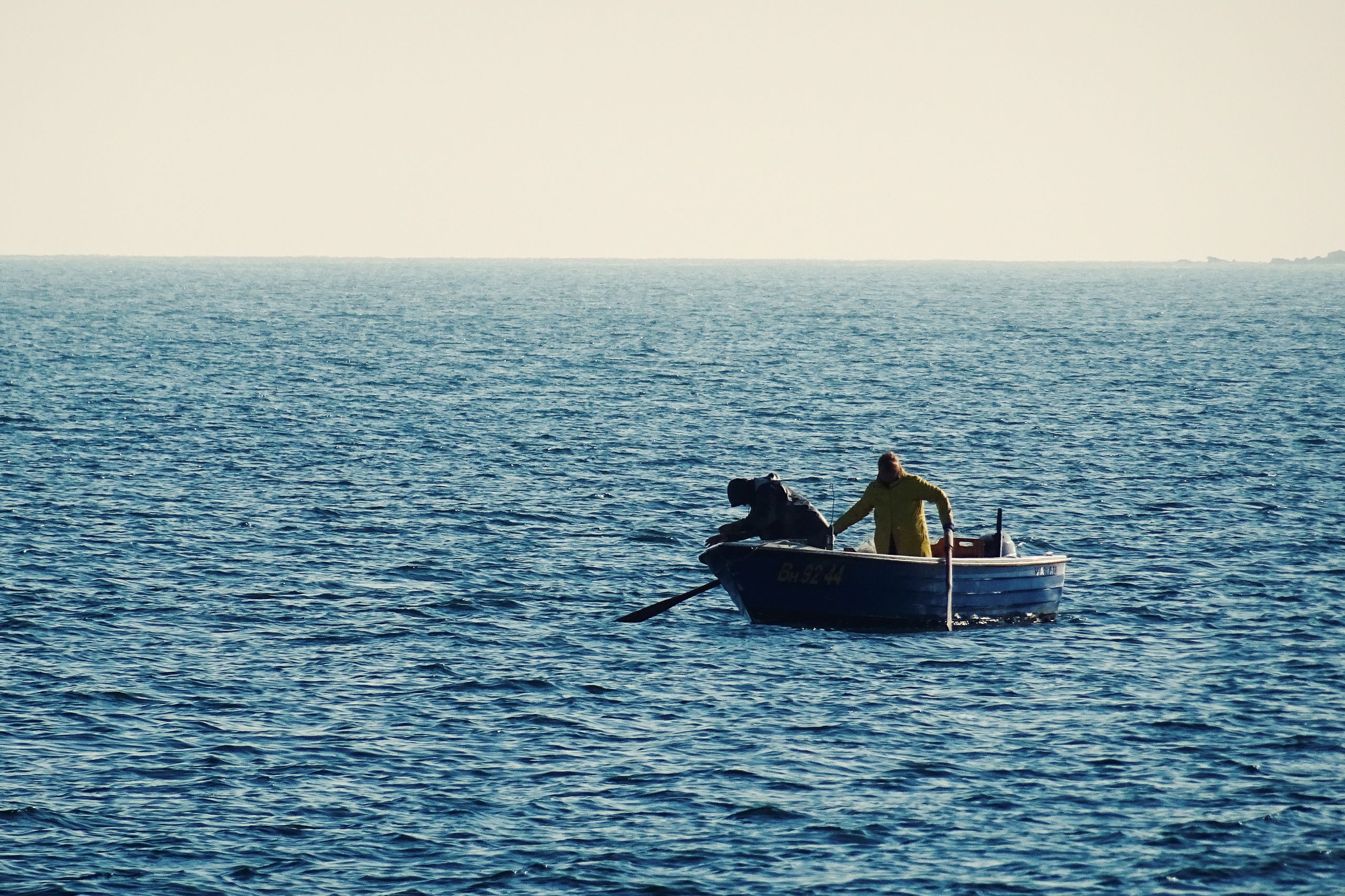 A lone person fishing in a small boat on a tranquil sea under a clear sky.
